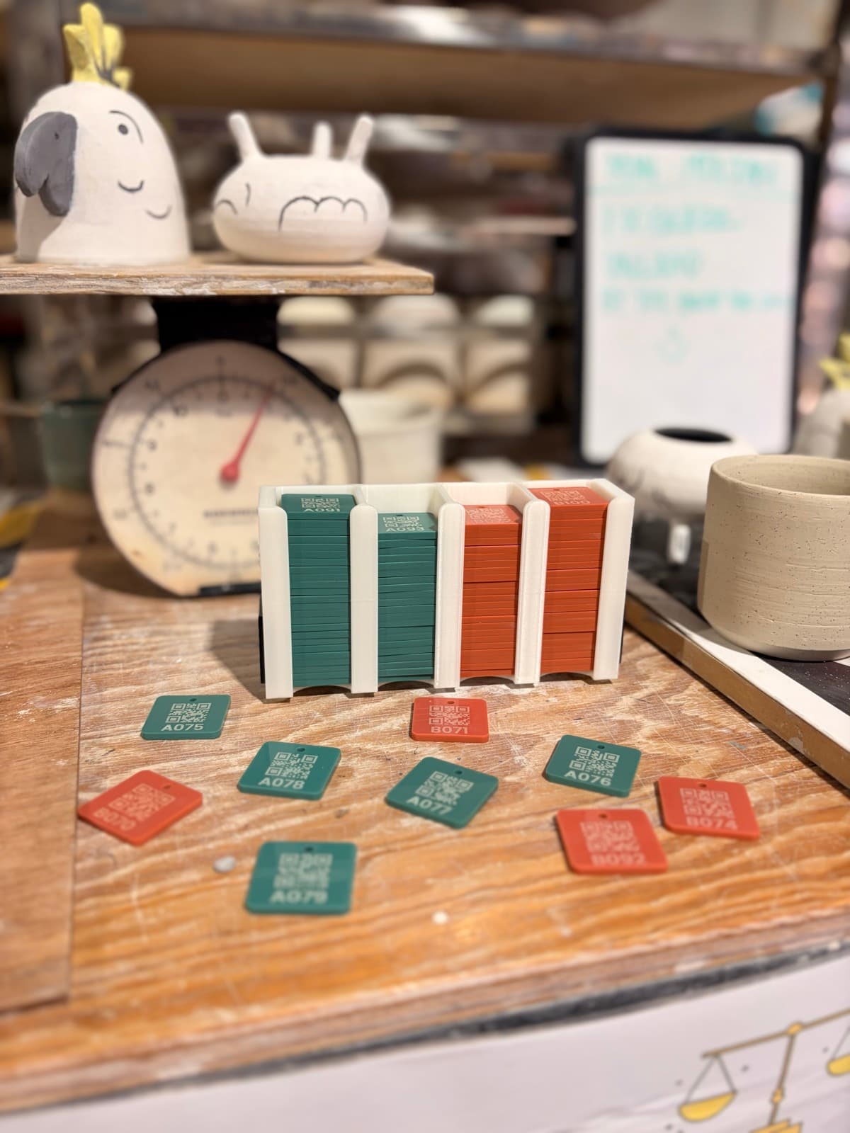 MudBuddy QR-coded tracking tiles in a pottery studio, with ceramic pieces and a kitchen scale in the background