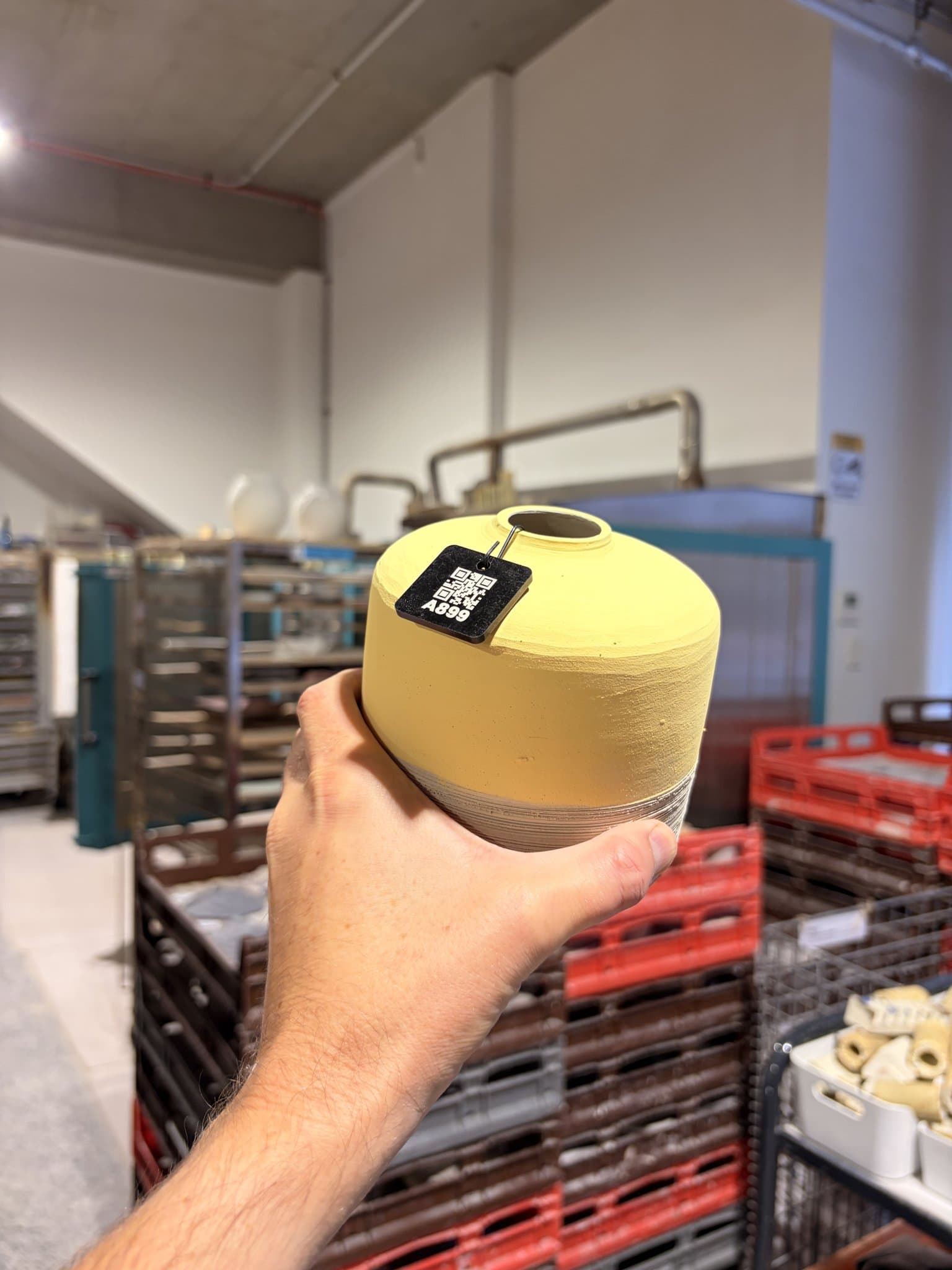 A finished pot with a MudBuddy QR tile attached, held in a studio.