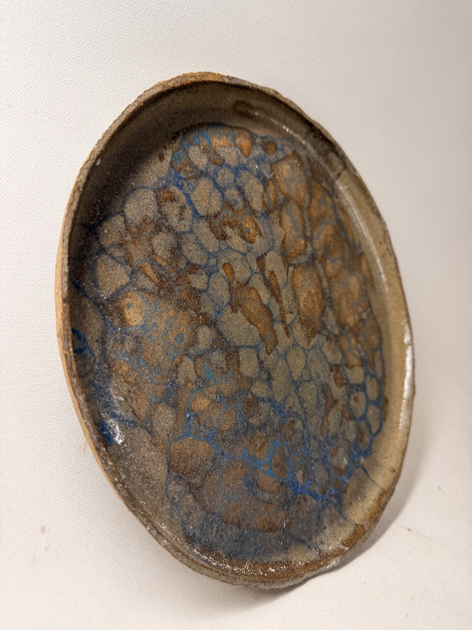 A finished handmade dish with a fired blue and tan crawl glaze.